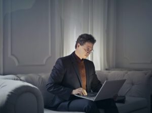 Man met bril zit op bank te werken achter laptop