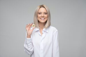 vrouw met blonde haren en witte blouse heeft bitcoin munt in hand